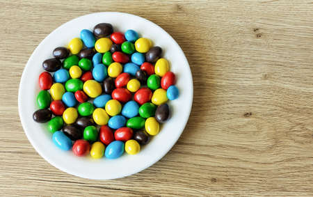 Peanuts in milk chocolate and sugar peel on a plate on a wooden ash table surfaceの写真素材