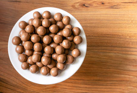 Maltesers milk chocolate balls on a plate on a pine tree surface, top viewの写真素材