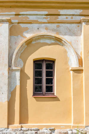 An old window on a collapsing yellow plastered painted wall with an arch
