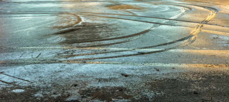 Blurred ice surface texture background at sunset on a paved site in winter with car tracksの写真素材