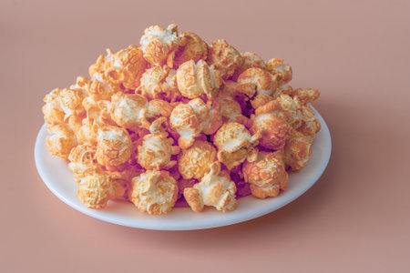 Image of popcorn with cheddar cheese flavor on a plate against a light brown backgroundの写真素材