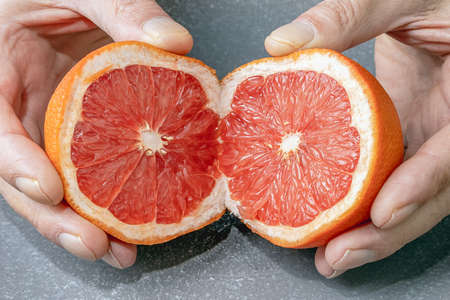 The grapefruit fruit is cut into two parts in the hands of the front viewの写真素材