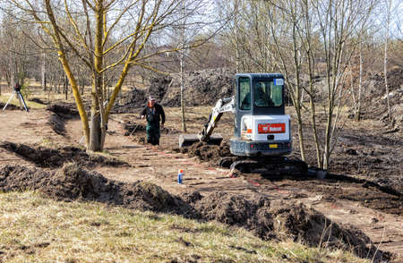 early spring small bobcat excavator with rubber tracks in the park digging the ground. Panevezys, Lithuania, April, 15 d.のeditorial素材
