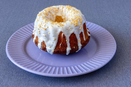 on a tablecloth on a plate a brown cupcake decorated with white icing and gold beads