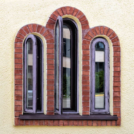 wooden antique window with three arches in yellow wall close up