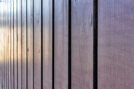 outdoor wooden fence vertical boards painted with brown paint from shadow against light, blurred focus in the distanceの写真素材