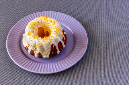 brown cupcake decorated with white frosting and gold beads on a plate on a tablecloth, top view
