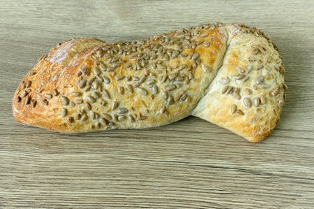 ciabatta bread wheat flour product with sunflower seed topping on oak table surface, side view