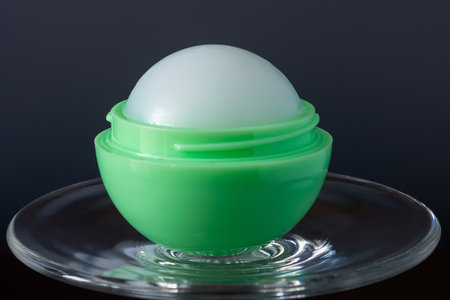 Female lip balm in green round ball on glass on dark background close up