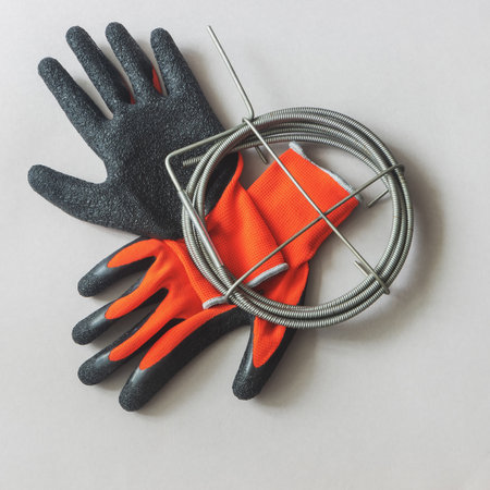 Metal cable for cleaning sewer pipes and knitted red gloves with black latex covered palms on gray background, top viewの写真素材