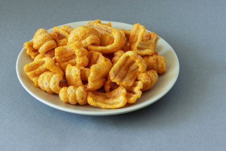 A pile of ham flavored puffed chips snacks on a plate on a gray background, close up