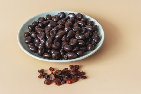 A close-up shot of a bowl filled with delicious dark chocolate covered raisins on an orange background. Color contrast gives the image vitality and attractiveness.の写真素材