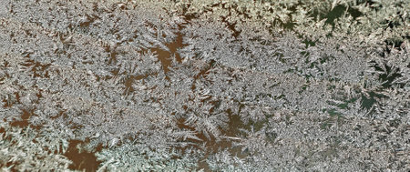 Delicate frost crystals form intricate patterns on a window, showing the art of nature. The chilly...
