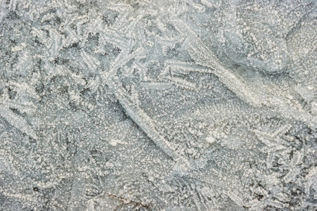 Delicate frost crystals form intricate patterns on the surface on a cold winter morning, showcasing...