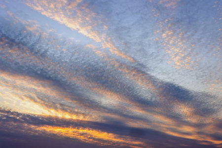Colors spread across the sky as the sun sets, casting warm hues of orange and purple. Wispy clouds create a beautiful pattern, enhancing the evening serenity.の写真素材
