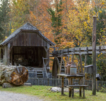 Three old milk cans on a table, water saw mill with visible water wheel in the background, autumn...