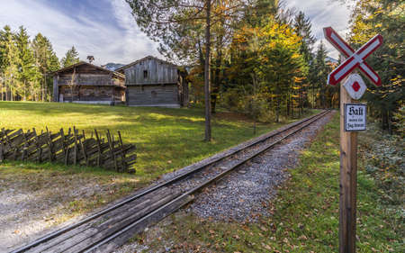 Historic ungated railroad crossing with german text - halt wenn ein zug kommt-  Old farmhouse and mountains in the background.の写真素材