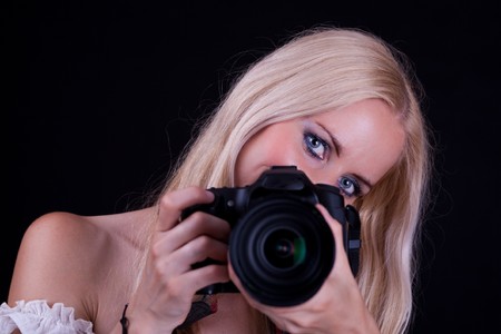 Blonde hair woman, holding camera aimed in front of you. Black Background.の写真素材