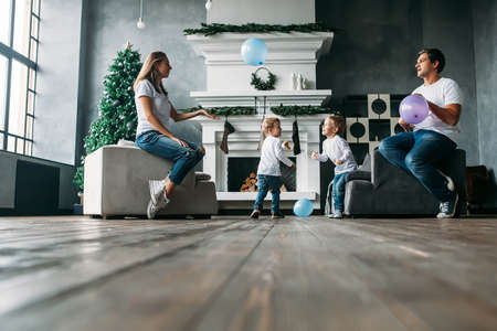 Father and mother siting on sofa playing air balloons with two little sonsの写真素材