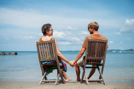 Family holding hands siting on the chairs tropical beachの写真素材