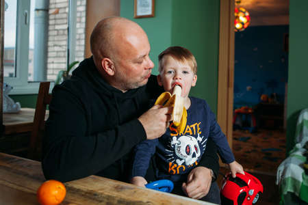 Father feeding his son with banana Boy with mouth openの写真素材