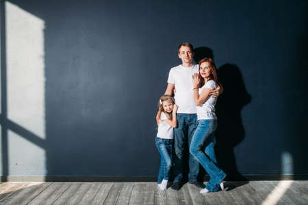 Happy family portrait standing on gray background wooden floor room window sunny dayの写真素材