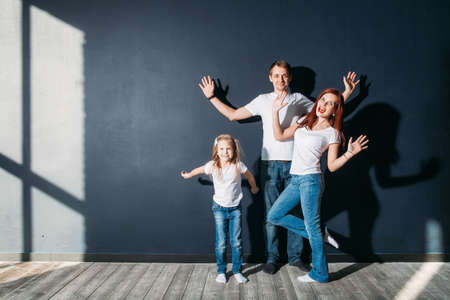Happy family portrait standing on gray background wooden floor room window sunny dayの写真素材