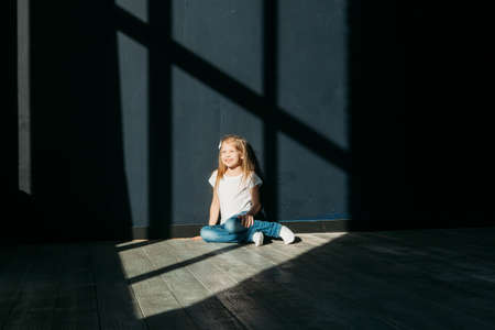 Happy girl portrait siting on gray background wooden floor room window sunny dayの写真素材