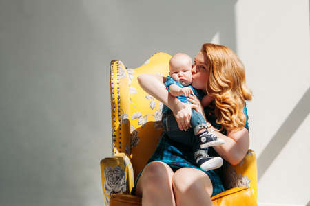 Family portrait photo of mother with his little son sit kissing and smiling in armchair on white backgroundの写真素材
