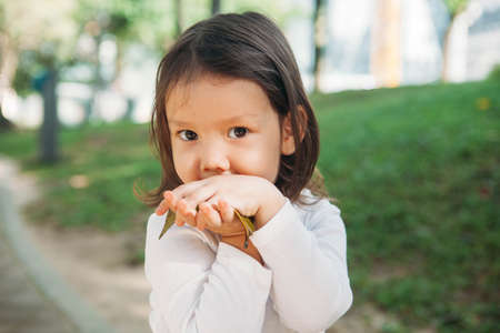 Young asian girl with green leave in autumn parkの写真素材