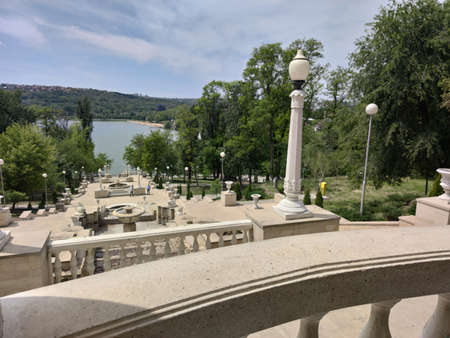 Stone stairs to the lake. Around the park with green trees and firs. White lanterns. Blue sky with cloudsの写真素材