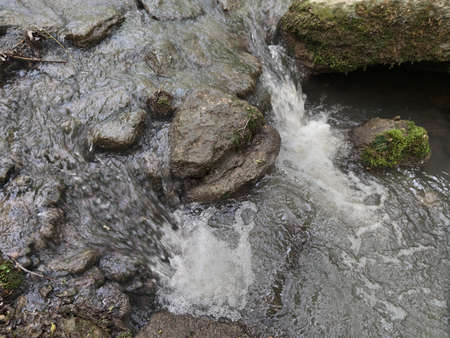 A small waterfall in a forest stream. Wet stones with green moss