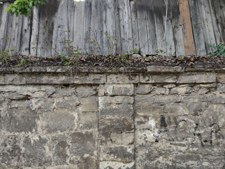 Old wall of gray large blocks with cement. Dry leaves and grass above. Old gray wooden boards. Kishinev. Moldovaの写真素材