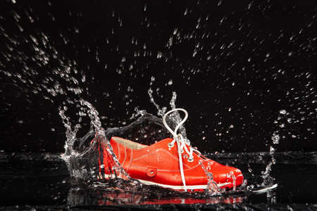 Red shoe falling in a water with splashes on a black backgroundの写真素材