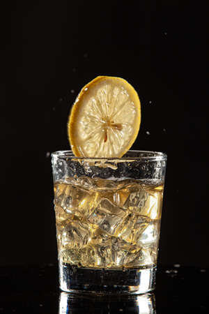Glass of beverage, ice and lemon on a black studio backgroundの写真素材
