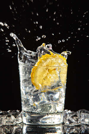 Glass of water, ice crystals and lemon on a black studio backgroundの写真素材