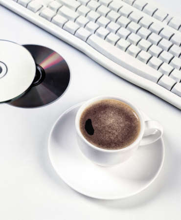 Cup of coffee compact discs and computer keyboard on an isolated studio background