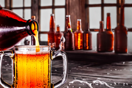 Glass of beer and different bottles on an old wooden barの素材