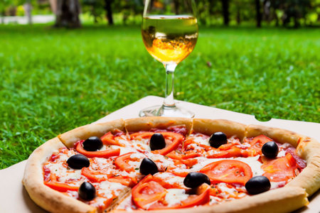 Pizza with ham, cheese and tomatoes on the green grass lawnの素材