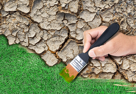 Black wooden paintbrush in hand and painting green grass on cracked soil in concept of conserve the environmentalの写真素材