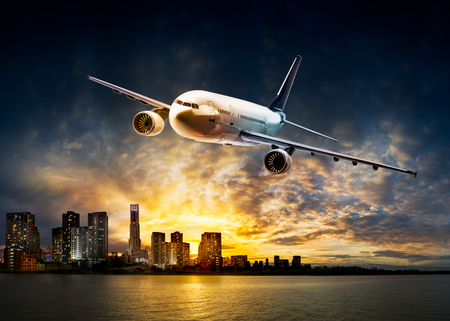 Airplane for transportation flying over the city at riverside and beautiful sunset backgroundの写真素材