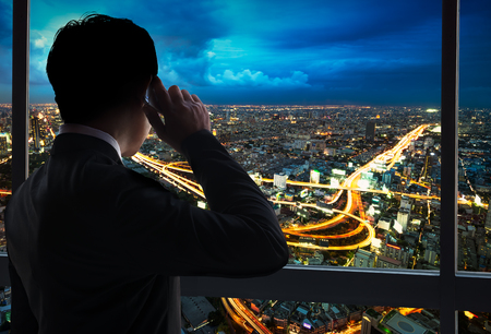 Business man using smart phone at glass window internal the building with night scene cityscape backgroundの写真素材