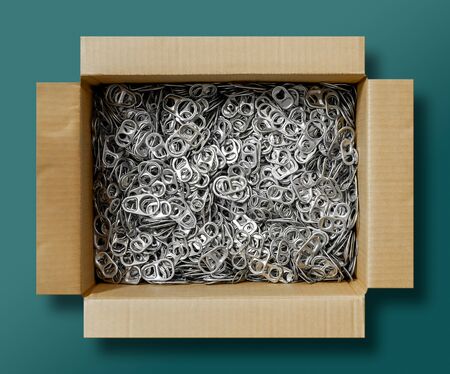 Aluminum ring pull can opener in brown, paper box on green background for recycling to make...