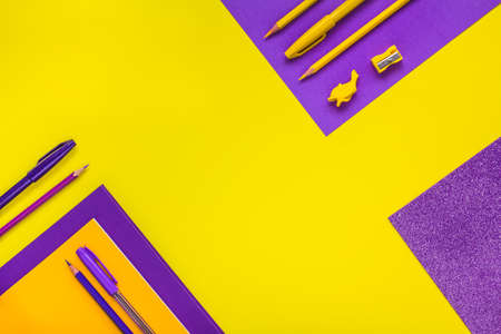 The concept of going back to school. Border frame of yellow and purple pencils, pens, markers on a...