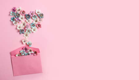 A heart shape of white, blue and pink flowers spills out of the envelope on a pink background. Valentines Day, love, congratulations. Pastel colors. Top view, banner, space for textの写真素材