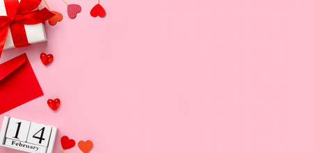 The concept of Valentines Day. A red envelope, hearts, a wooden calendar with a date and a white gift with a satin ribbon on a pink background. Banner. Flat lay, copy spaceの写真素材