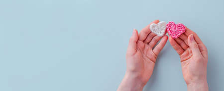 Valentines day background. Womens hands hold two linked hearts of white and pink color from threads on a blue background. Close-up. The concept of a holiday and relationships. Flat lay, copy spaceの写真素材