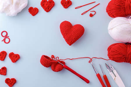 Knitted hearts in red and white, knitting tools, yarn and hook on a blue background. Valentines Day,...