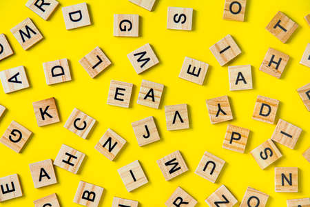 The concept of developing thinking, grammar, back to school, learning. Top view of square wooden tiles with the English alphabet lying on a yellow background.の写真素材