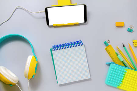 Online training during the epidemic. The concept of back to school in a new format. Yellow and blue stationery, headphones, phone on a gray backgroundの写真素材
